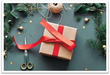Holiday gift box wrapped in plain brown paper, with ribbon, pine needles, leaves, baubles, twine, and scissors